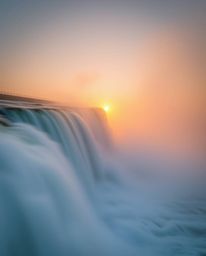 A dynamic motion scene of a sun setting behind a dramatic waterfall. The image is characterized by thick fog, blurred lines, 