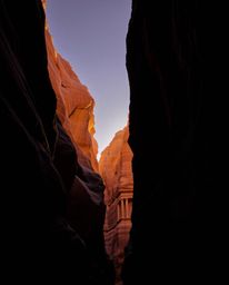 A stunning display of high-contrast, low-key lighting illuminates sandstone cliffs at sunset within a deep canyon. This speci