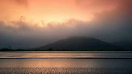A captivating low-angle shot captures a mesmerizing sunset over fog-covered hills, drenched in a gentle drizzle. The image sh