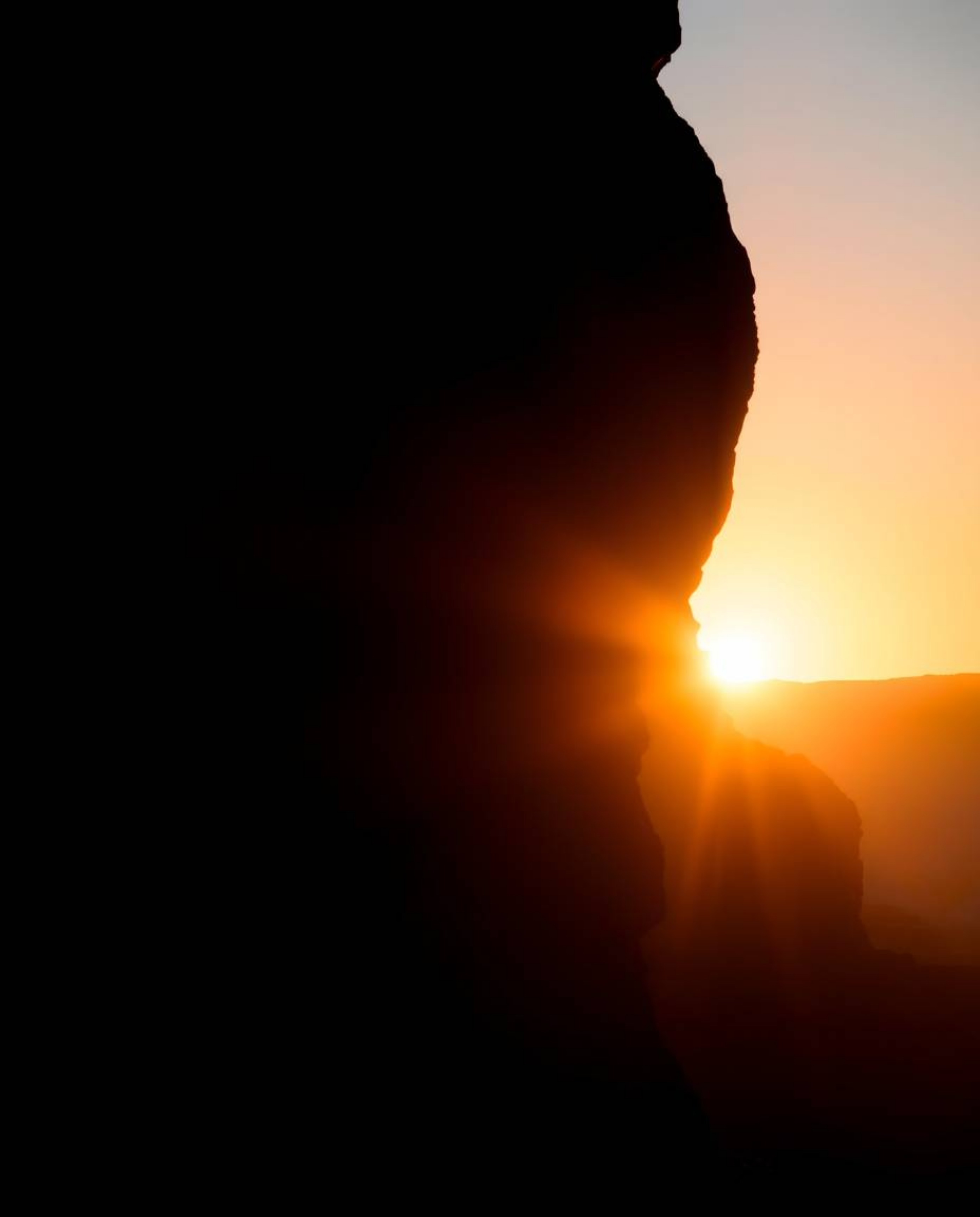 A silhouetted image, created using dramatic backlighting, depicts a sunset illuminating sandstone cliffs in a canyon. The art