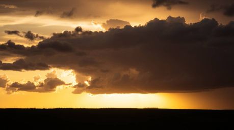Witness the breathtaking spectacle of thunderstorm clouds silhouetted against a vibrant sunset.  Backlighting creates a stunn