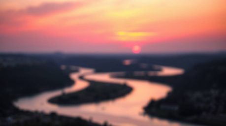 A captivating image of a winding river bathed in the dramatic glow of an orange-pink sunset.  The photograph employs a blurre