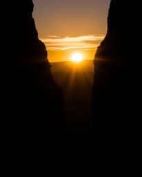 An intensely backlit silhouette in jet black depicts a sunset illuminating sandstone cliffs in a canyon. This striking image 