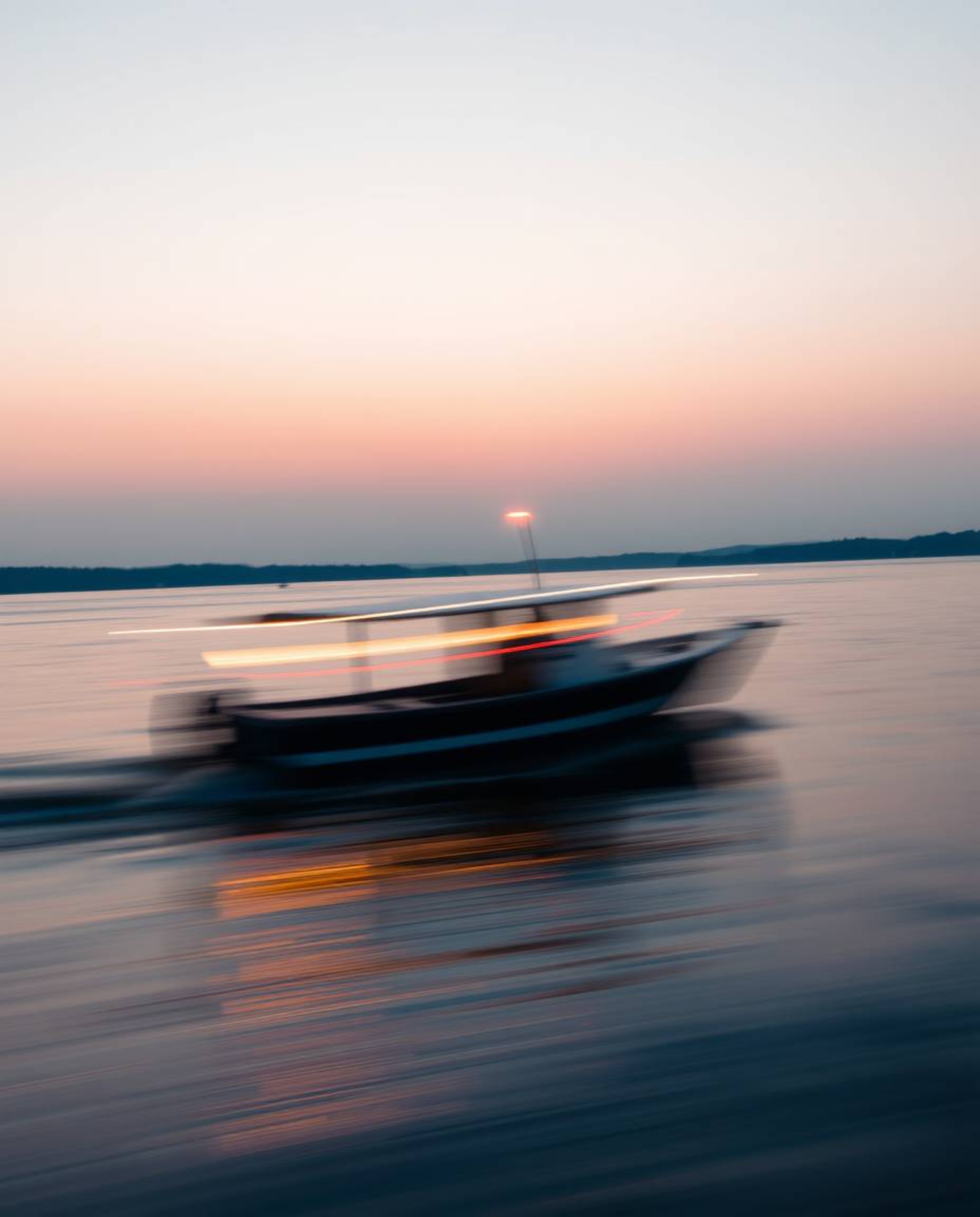 A long-exposure photograph of a boat drifting on a lake at sunset beautifully captures both light trails and motion blur. Thi