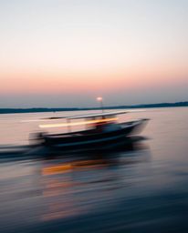 A long-exposure photograph of a boat drifting on a lake at sunset beautifully captures both light trails and motion blur. Thi