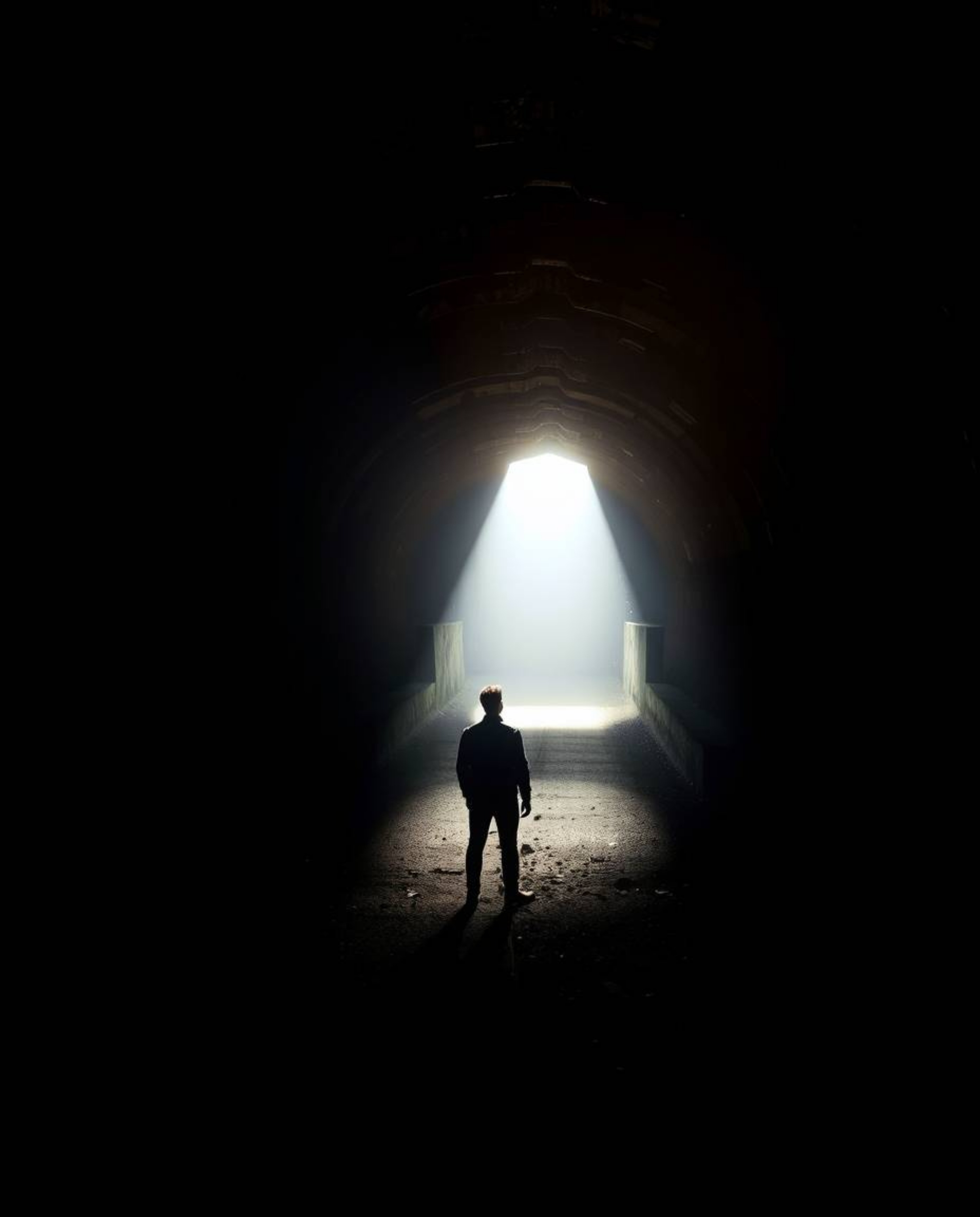 A captivating high-resolution stock photo depicting a person standing at the edge of a tunnel, gazing towards a bright light.