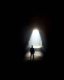 A captivating high-resolution stock photo depicting a person standing at the edge of a tunnel, gazing towards a bright light.