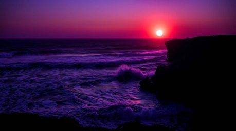 Experience the breathtaking beauty of waves crashing against cliffs under a vibrant sunset.  Deep ultraviolet hues and vivid 