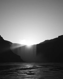 This is a timeless and elegant black and white photograph featuring a dramatic waterfall beautifully silhouetted against a se