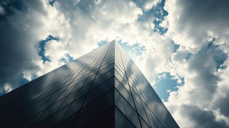 A captivating low-angle shot depicts a modern glass building seemingly dissolving into a soft, cloudy sky.  The image utilize