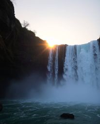 An adorable and charming scene of a Sun setting behind a dramatic waterfall, with cute features emphasized to create a whimsi