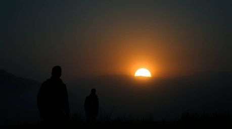 A captivating image of silhouetted figures against a breathtaking sunset piercing through a fog-covered landscape.  The dark 