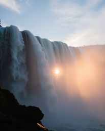 This tight close-up shot captures a mystic and enchanting environment as a sun sets behind a dramatic waterfall. The composit