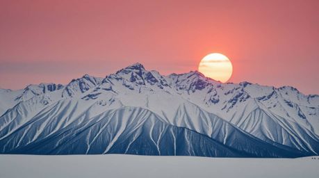 A captivating 16:9 landscape photograph showcasing snow-covered mountains bathed in the soft glow of a pastel sunset. The ima