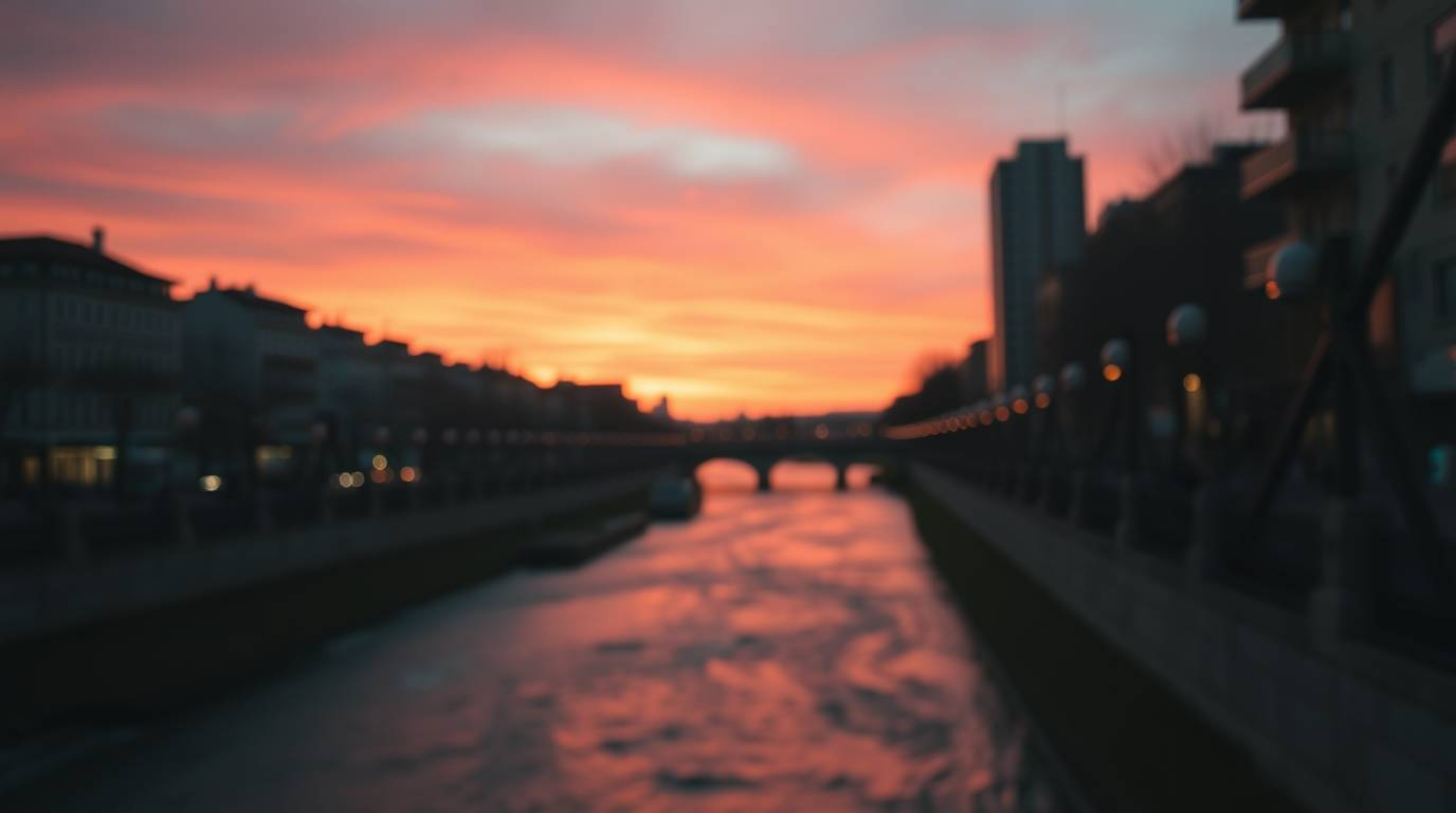 A captivating close-up street photograph showcases a winding river bathed in the warm glow of a dramatic orange-pink sunset. 
