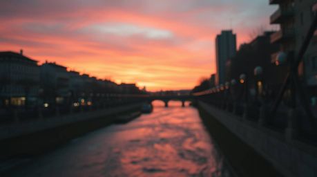A captivating close-up street photograph showcases a winding river bathed in the warm glow of a dramatic orange-pink sunset. 