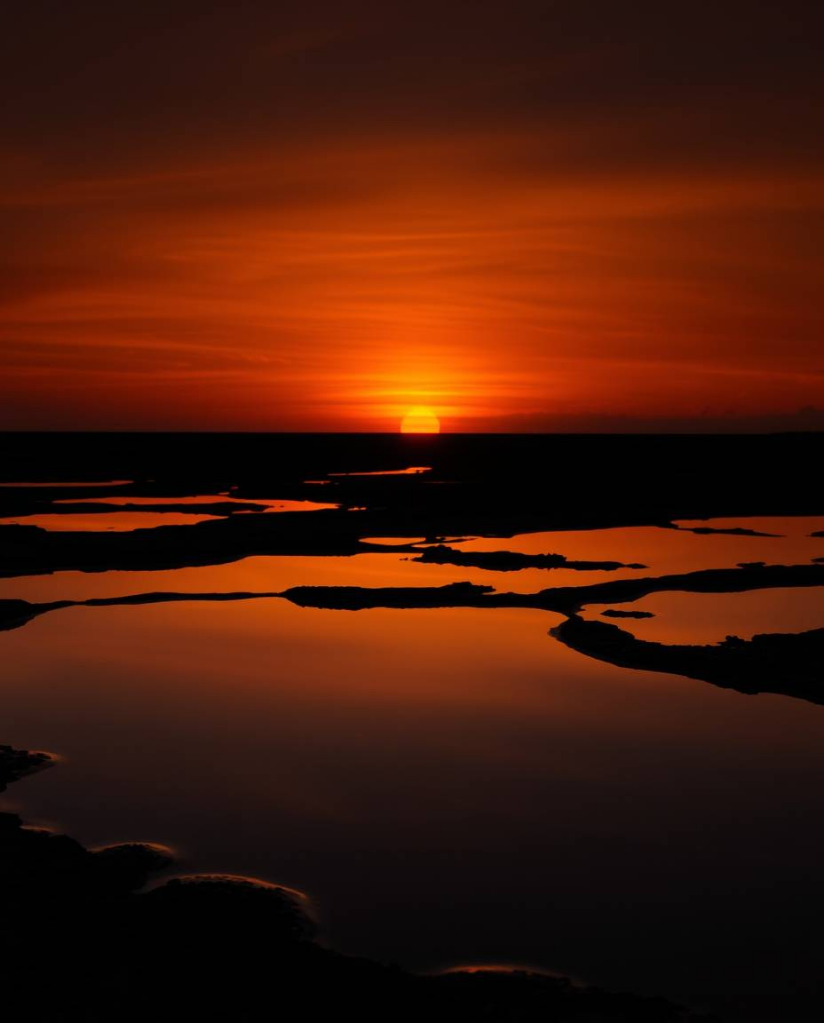 A high-contrast, low-key professional photograph of Photo of the Year caliber depicts a sunset sky mirrored in tidal pools. F
