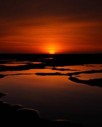A high-contrast, low-key professional photograph of Photo of the Year caliber depicts a sunset sky mirrored in tidal pools. F