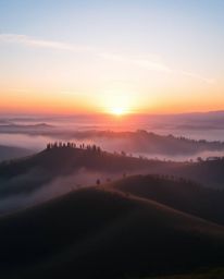 A breathtaking sunset over misty Tuscan hills, captured in a photograph with iridescent colors reflecting the warm golden hou