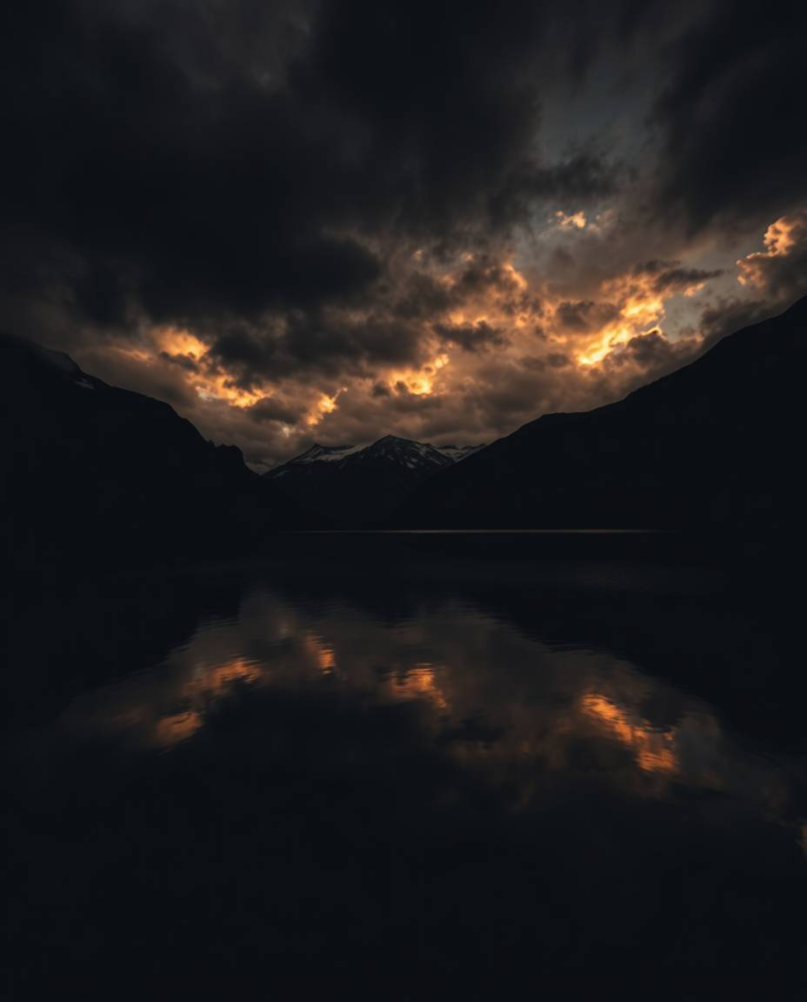A photograph utilizing high-contrast, low-key lighting to capture the reflections of fiery clouds in a mountain lake. This te