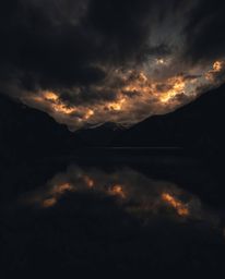 A photograph utilizing high-contrast, low-key lighting to capture the reflections of fiery clouds in a mountain lake. This te