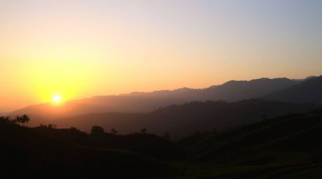 Witness the breathtaking beauty of silhouetted rice terraces nestled in the mountains against a vibrant sunset. This captivat