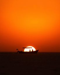 A silhouetted boat is seen drifting on a sunset lake, perfectly backlit by a light source positioned behind the subject. This