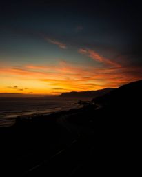 This artwork is a strong, moody style depiction of creative light art, featuring a sunset sky over a winding coastal highway.