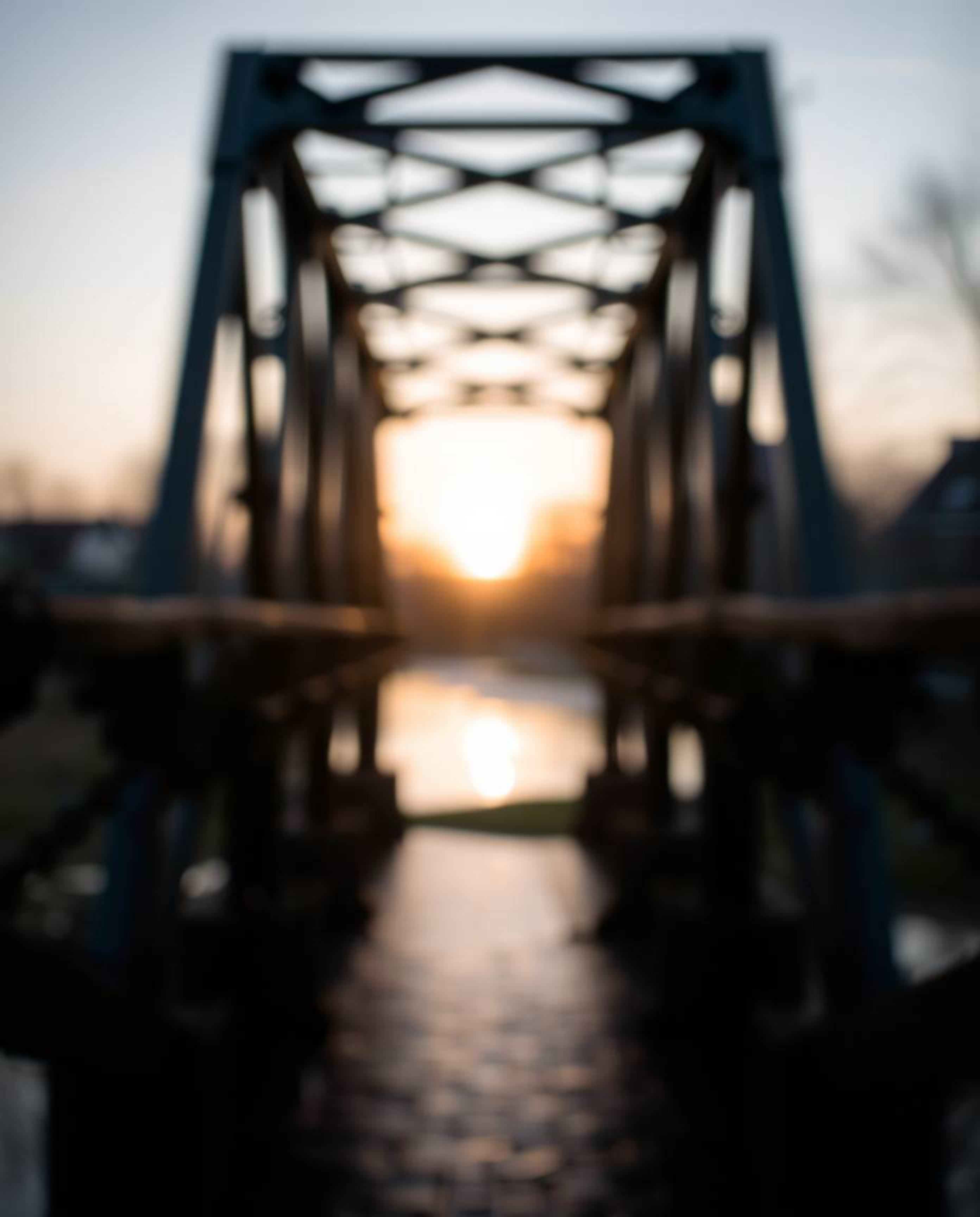 An old wooden bridge over a river at sunset is captured with a sharp subject focus, beautifully isolating it against a soft b