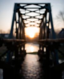 An old wooden bridge over a river at sunset is captured with a sharp subject focus, beautifully isolating it against a soft b