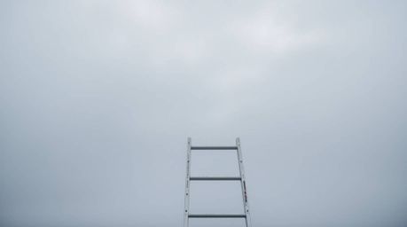 A minimalist scene featuring a close-up of a silver ladder enveloped in thick fog, set against the backdrop of an open field 