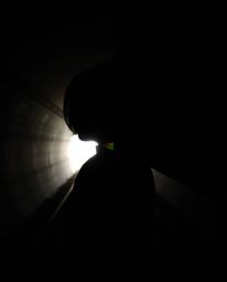 A striking image featuring a person with dark hair silhouetted against the bright light at the end of a tunnel. The image is 