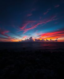 An image of a colorful sky over a coral reef at low tide, bathed in intense jet black. Warm candlelight provides the only ill