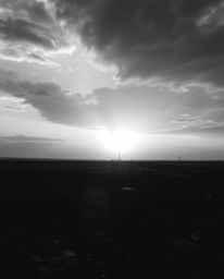 A captivating black and white fine art photograph portrays a sunrise over a desolate, war-torn landscape.  The unusual compos