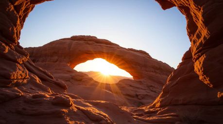 Experience the magic of the desert with a stunning low-angle photograph capturing a breathtaking sunset through a natural roc