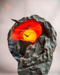 This is a sculptural clay artwork that captures a dynamic sunset over a coastal cliff, featuring soaring birds in motion. The