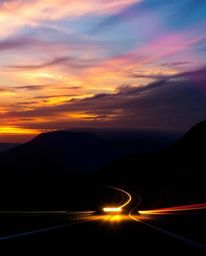 This creative light art piece captures a sunset sky over a winding coastal highway from a dynamic low-angle perspective, look