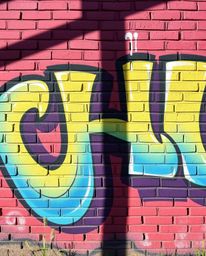 A vibrant graffiti artwork explodes across a brick wall, showcasing smooth gradient transitions, strong hard light, and drama