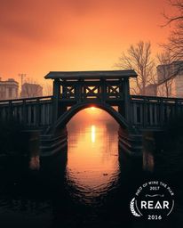 A professional, Photo of the Year style photograph captures an old wooden bridge over a river at sunset, creating a truly eth