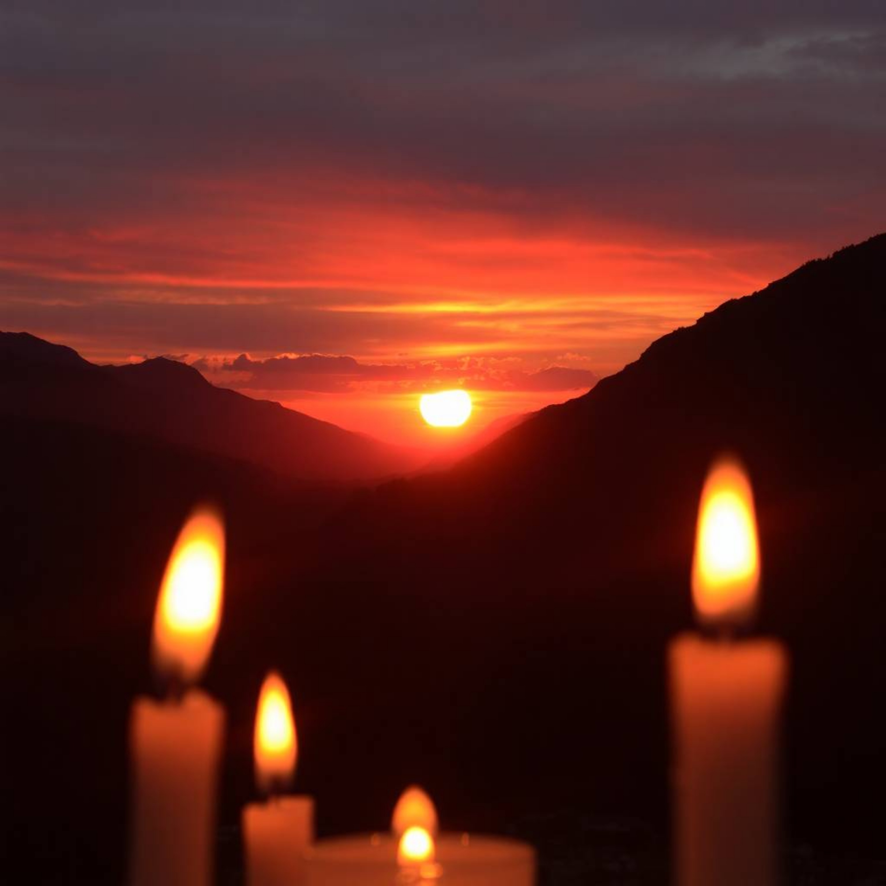 Capture the serene beauty of a sunset over a quiet mountain valley, enhanced by the warm, inviting glow of candlelight and th