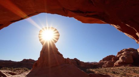 A captivating low-angle photograph captures a vibrant sunset viewed through a majestic desert rock arch. The image showcases 