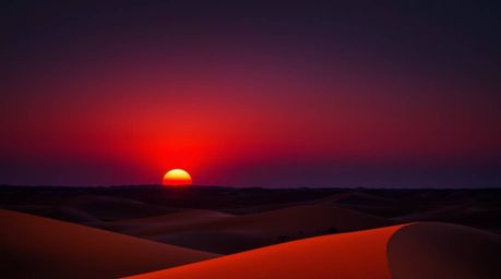A captivating long exposure photograph captures the vibrant hues of a sunset over golden desert dunes. Rich burgundy and deep