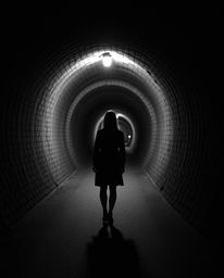 A captivating black and white photograph depicts a person in a timeless pose standing at the edge of a tunnel, gazing towards