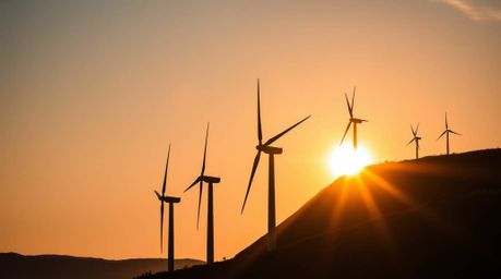 A captivating architectural color photograph featuring a low-angle view of wind turbines silhouetted against a vibrant sunset