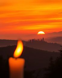 High-resolution stock photo: warm sunset over misty Tuscan hills, reds oranges yellows, flickering candlelight, warm glow, co