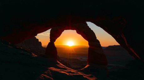 Experience the breathtaking beauty of a desert sunset viewed through a natural rock arch. Rich, deep teal tones and silhouett
