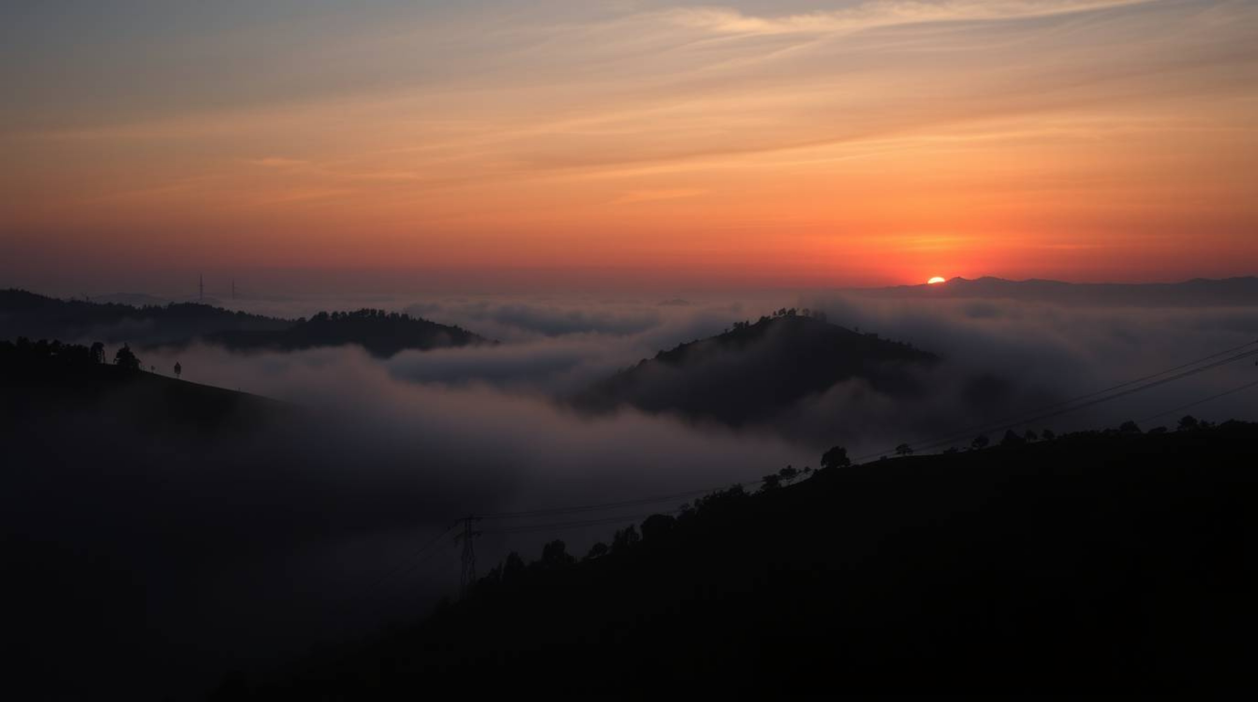 An image depicting fog-covered hills bathed in the light of a setting sun, rendered with smooth gradient transitions and stri
