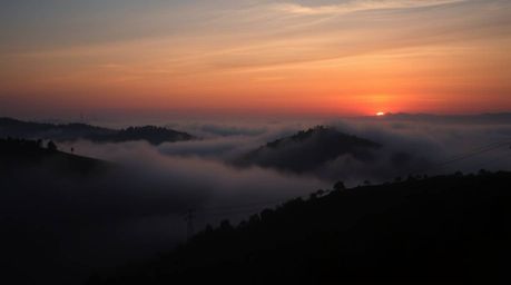 An image depicting fog-covered hills bathed in the light of a setting sun, rendered with smooth gradient transitions and stri