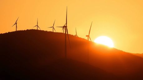 A captivating image showcasing a breathtaking sunset behind a row of wind turbines perched atop a hill.  The warm golden ligh