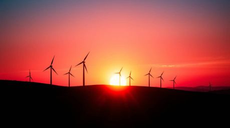 A breathtaking sunset view behind a row of wind turbines perched atop a hill, captured with striking burgundy and deep blue t